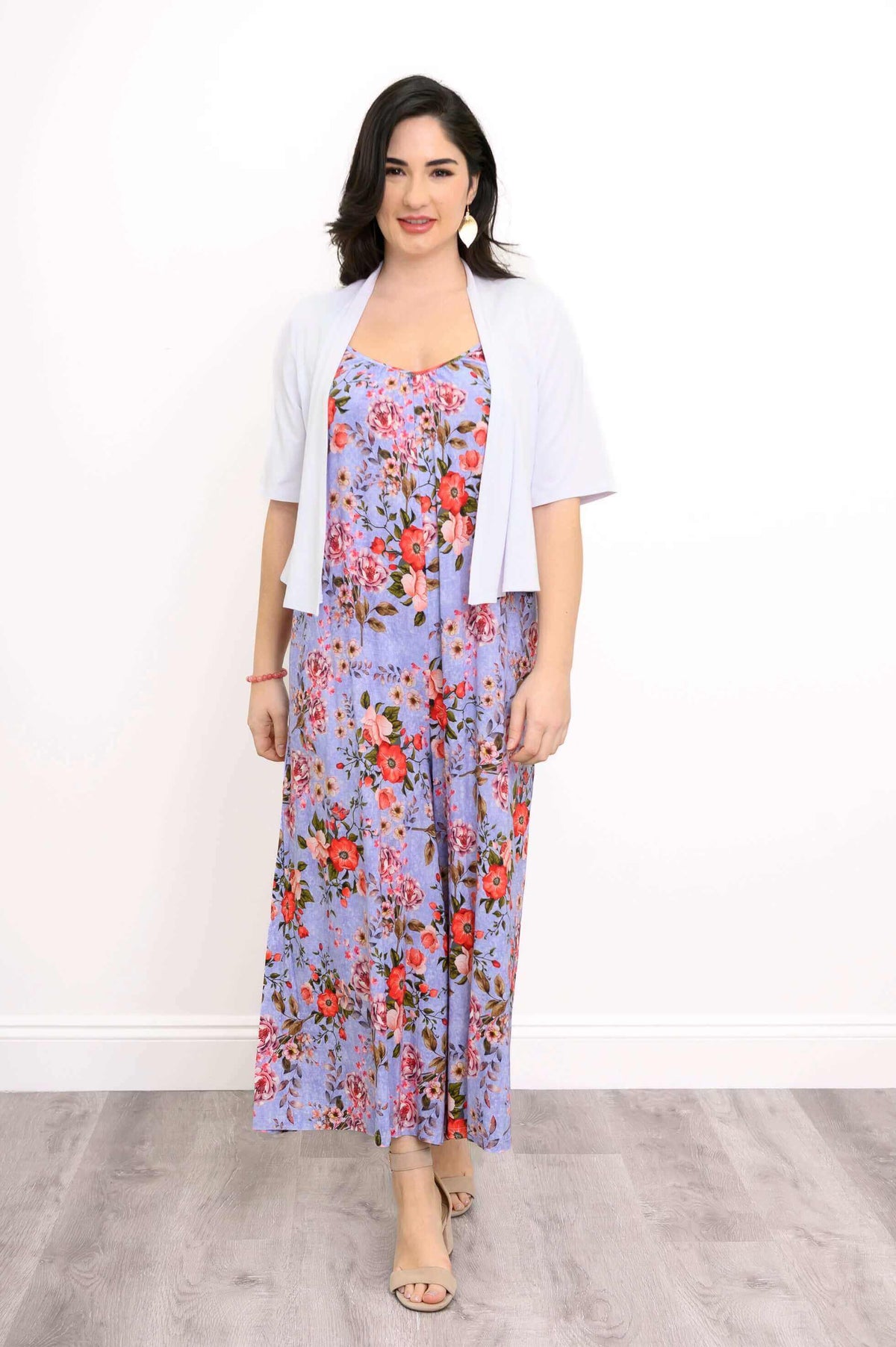 Woman in lavender floral maxi dress with a light cardigan, standing in front of a white wall