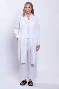 Model layering a long white striped duster over matching pants and top
