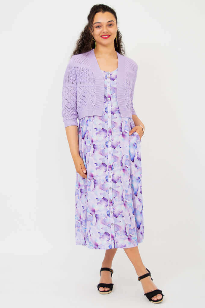 Model posing with hands in pockets wearing lilac cropped cardigan and purple patterned dress