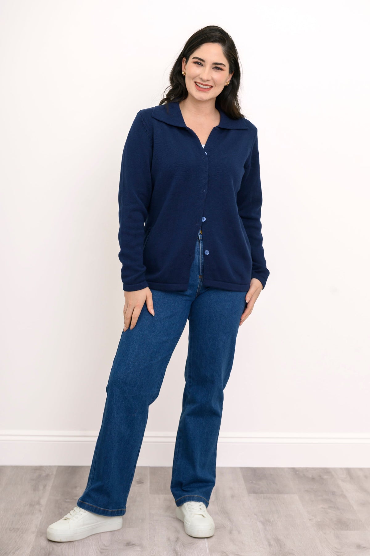Front view of a woman wearing a classic buttoned navy knit shirt sweater styled with dark blue denim.