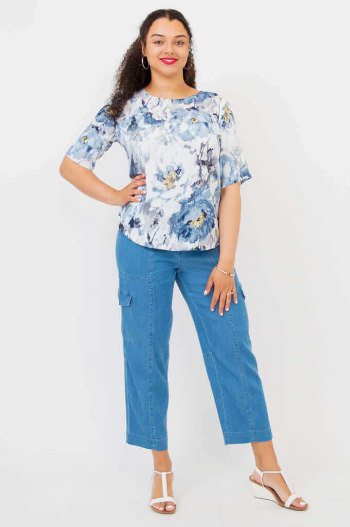 Full body view of model posing in Liza floral blouse with one hand on hip, blue cargo-style pants
