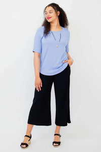 Model looking left in light blue blouse, hand in pocket, with black pants