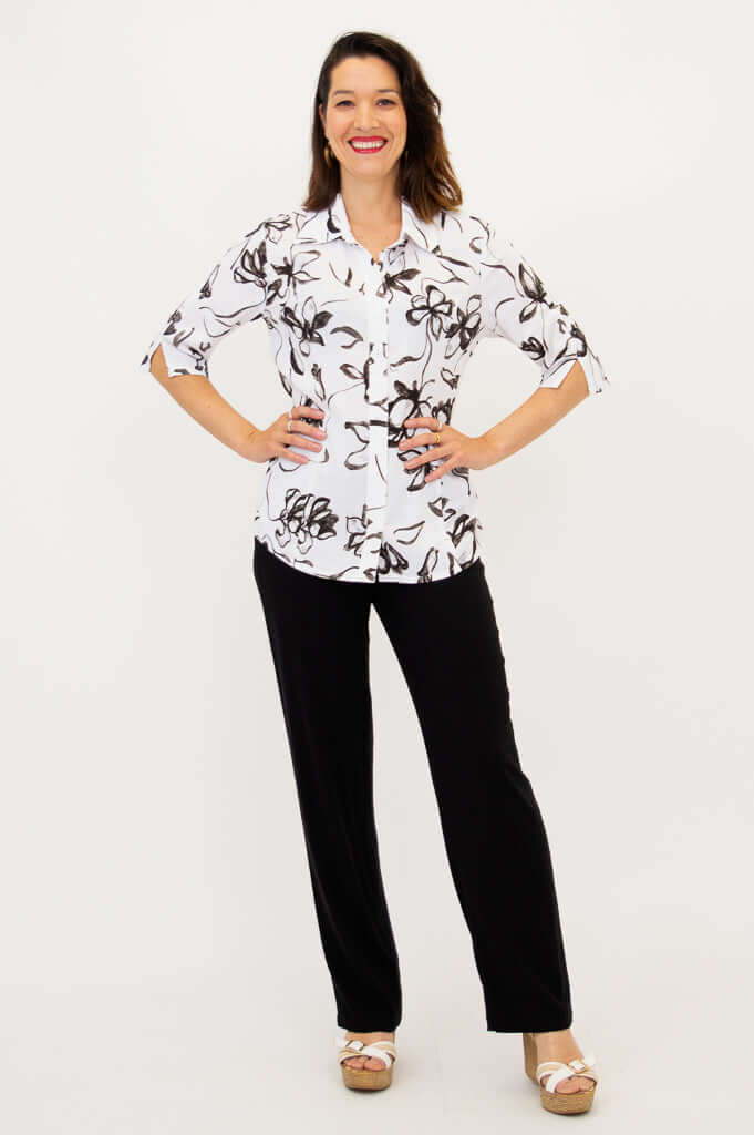 Woman posing with hands on hips in white blouse with black floral print and black pants