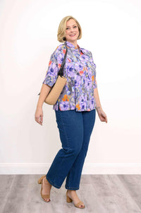 Angled view of woman wearing Lorine floral blouse with handbag and blue jeans