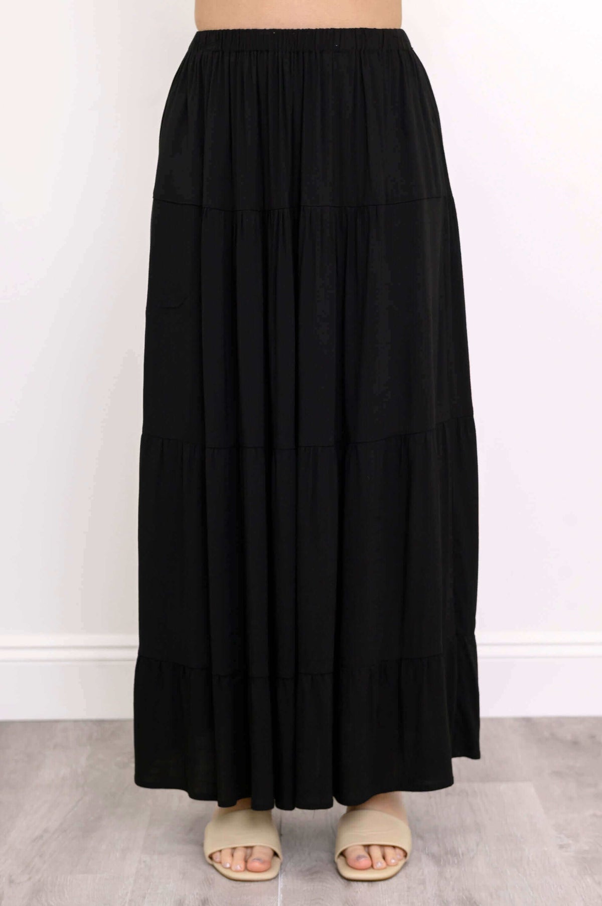 Detailed view of the lower half of the black maxi skirt and beige sandals