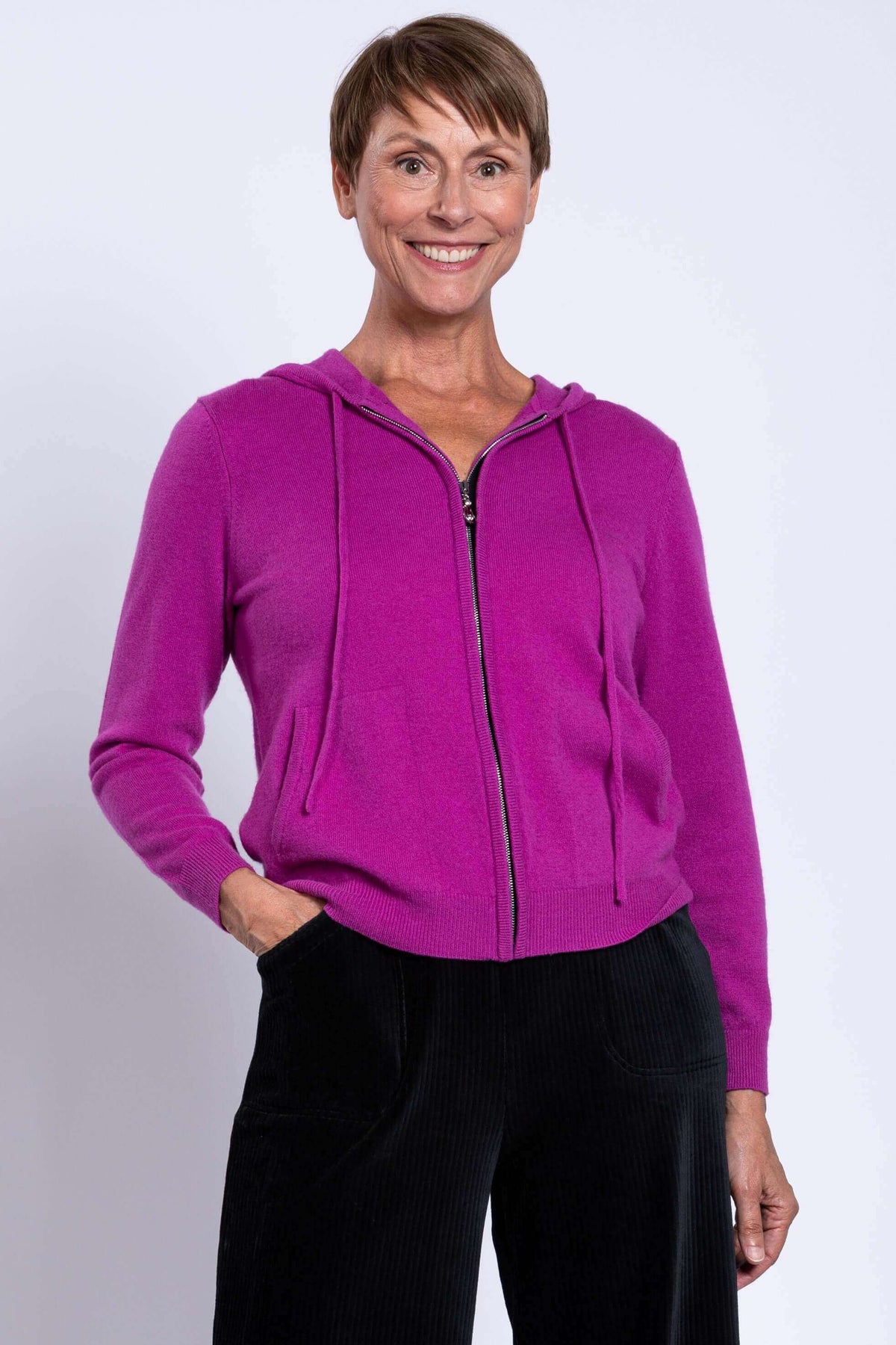 Studio portrait of a model modeling a bright magenta pink long sleeve hooded cardigan with zip closure.