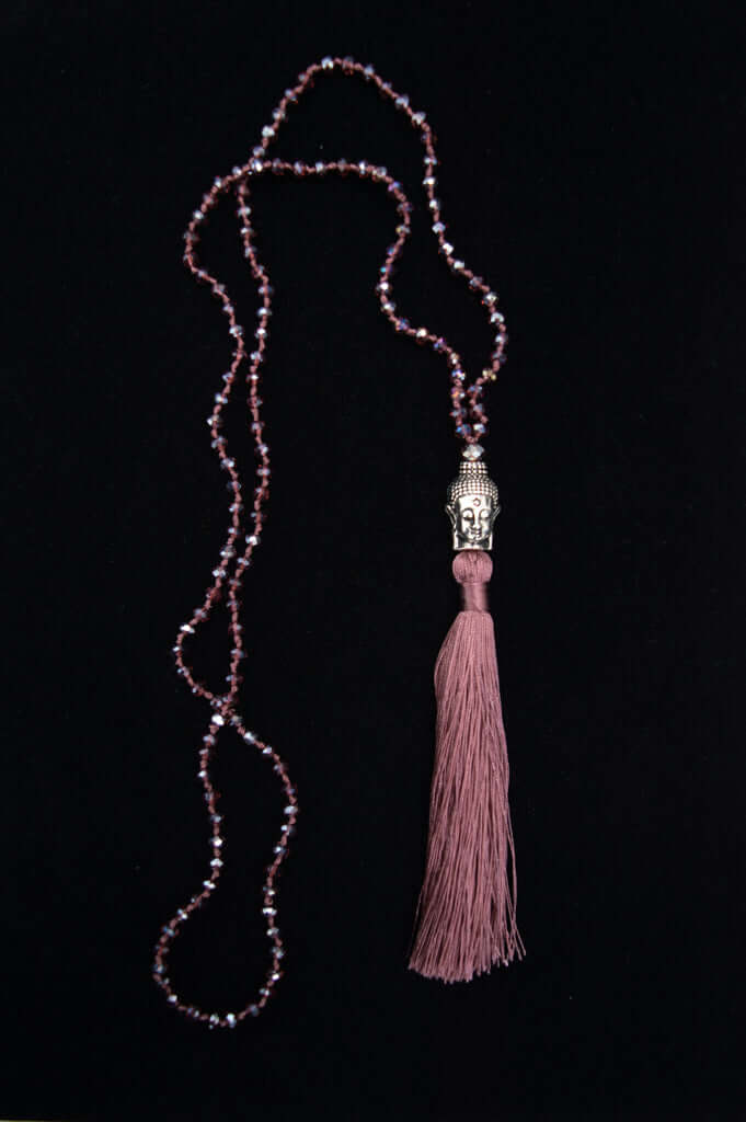 Mala necklace with purple beads, a silver Buddha head, and a purple tassel on black background