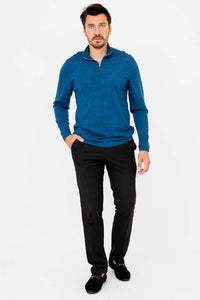 Man standing with hands in pockets in a blue merino sweater and black pants
