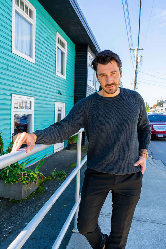 Man in charcoal ribbed sweater leaning on a railing outdoors