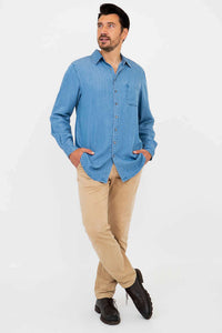 Man crossing legs, hands in pockets, displaying light blue button-up shirt