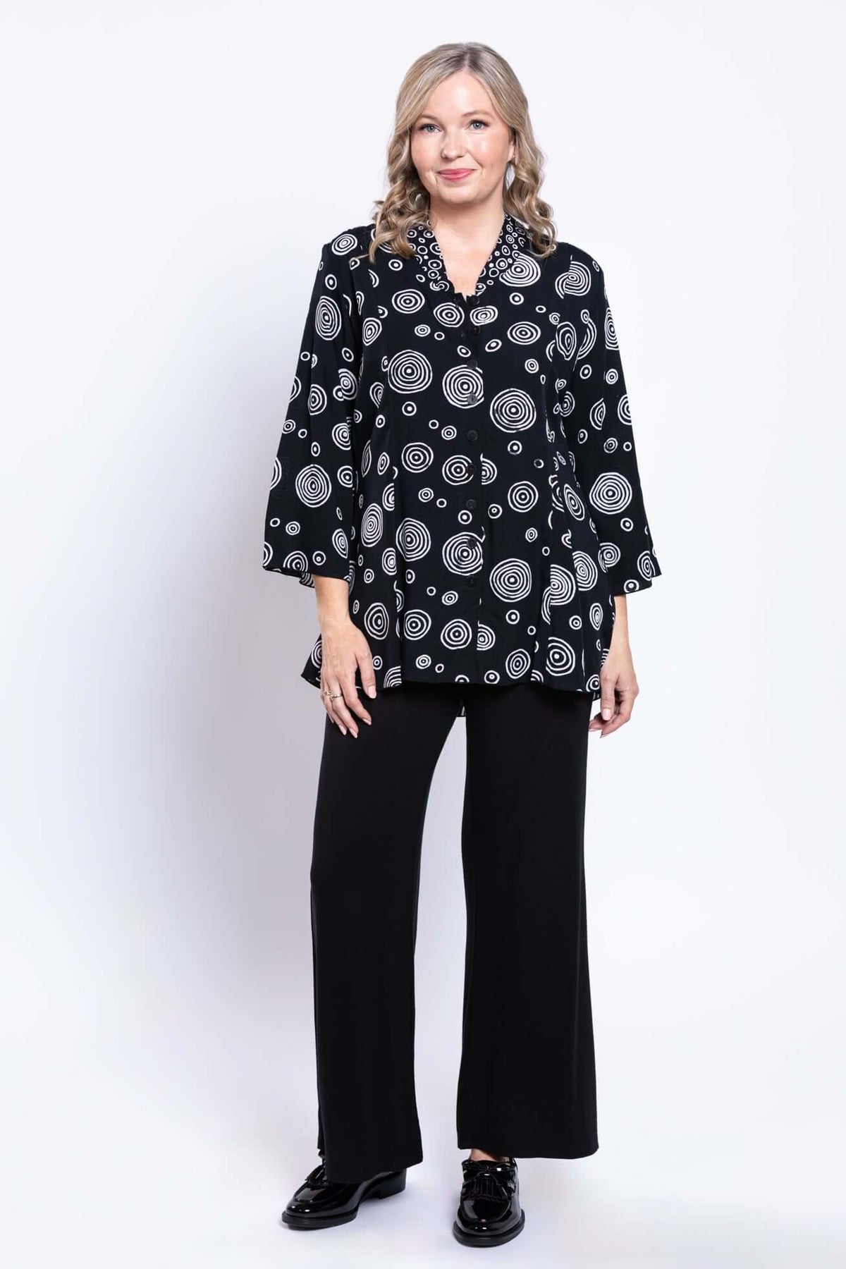 Model posing in black blouse with white concentric circles and matching black pants