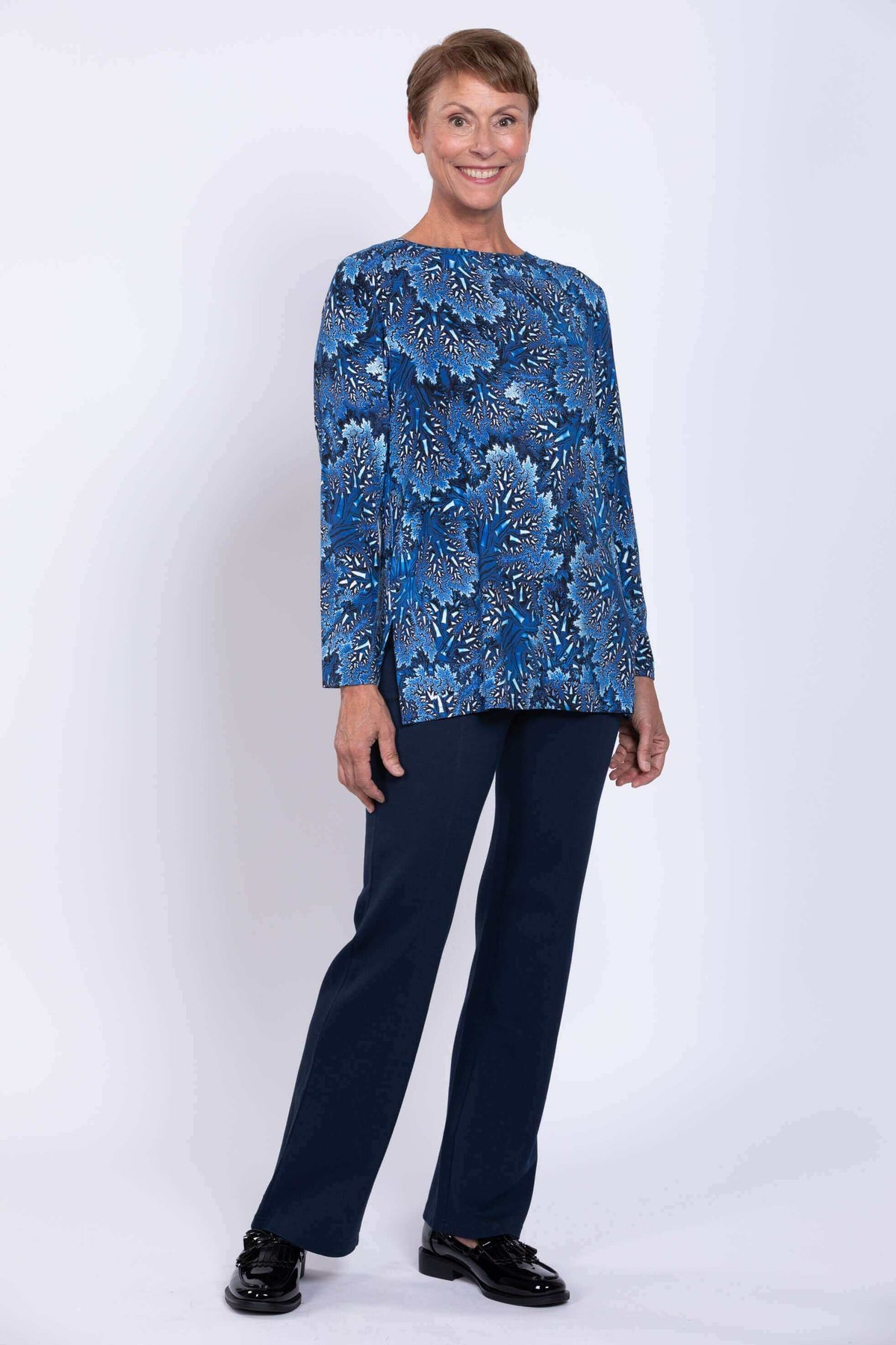 Woman in blue coral print long top standing in navy pants