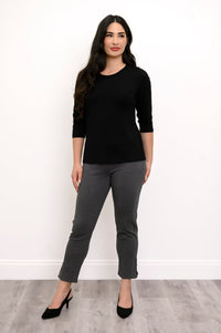 Full body front view of woman wearing black long sleeve shirt, grey pants, and black heels