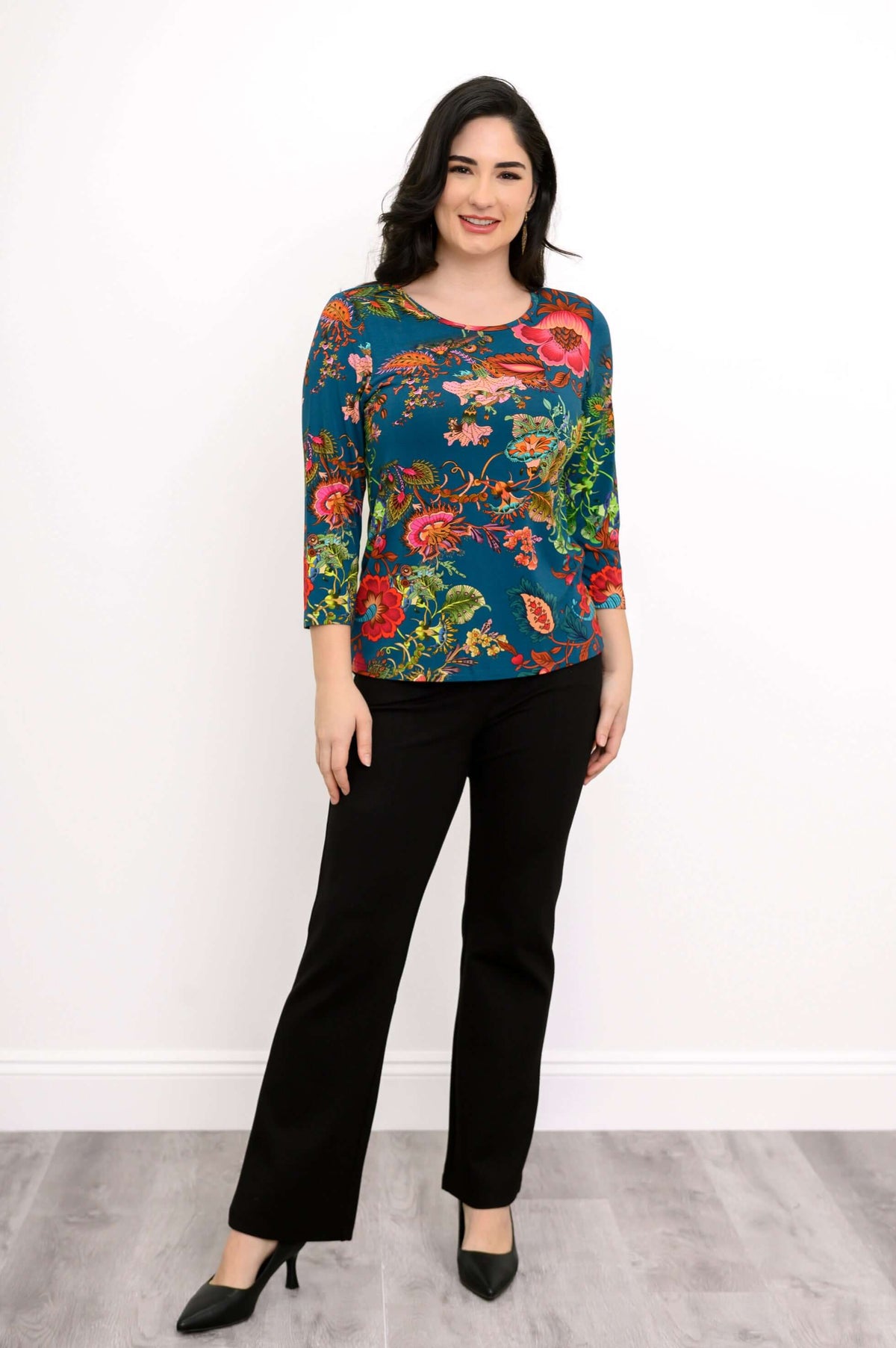 Woman standing and smiling in teal floral bamboo tee and black dress pants