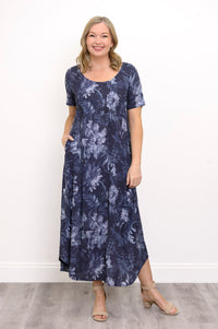 Front view of woman wearing long navy blue floral dress with pockets and sandals on a white background