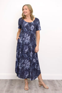 Front view of woman wearing long navy blue floral dress with pockets and sandals on a white background
