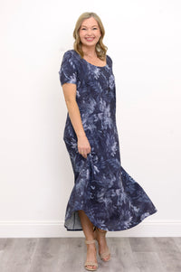Front view of woman wearing long navy blue floral dress with pockets and sandals on a white background