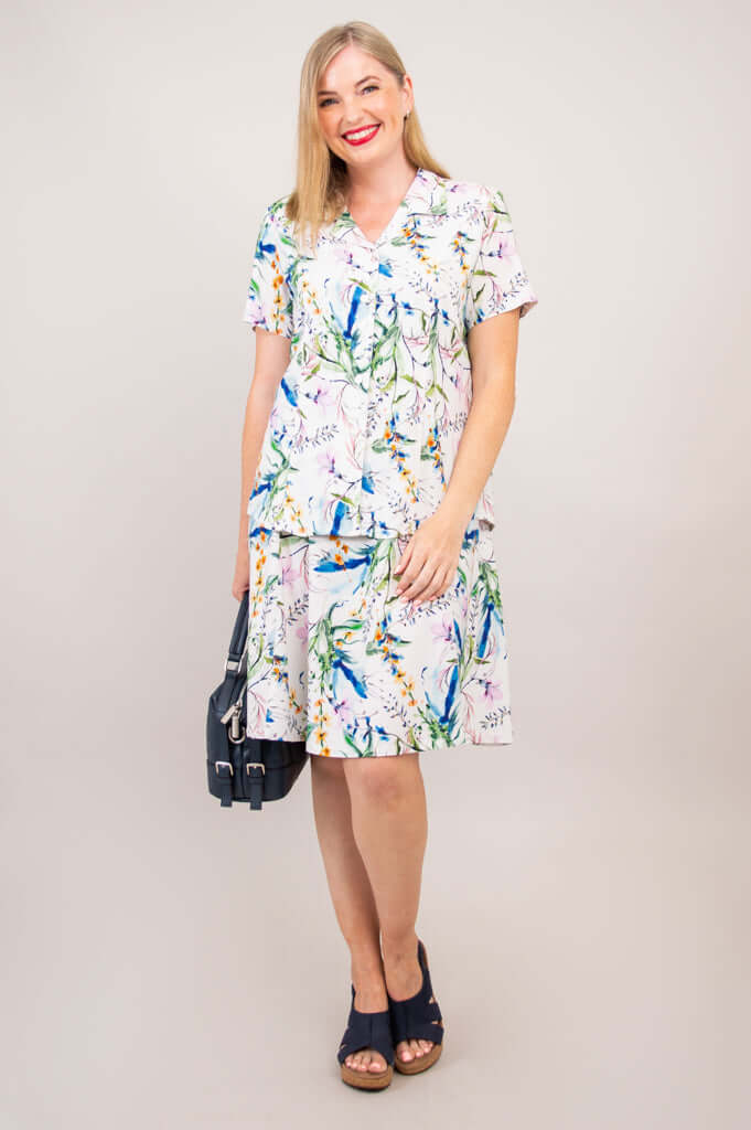Woman in a matching set with floral shirt and skirt, holding a navy handbag, front view