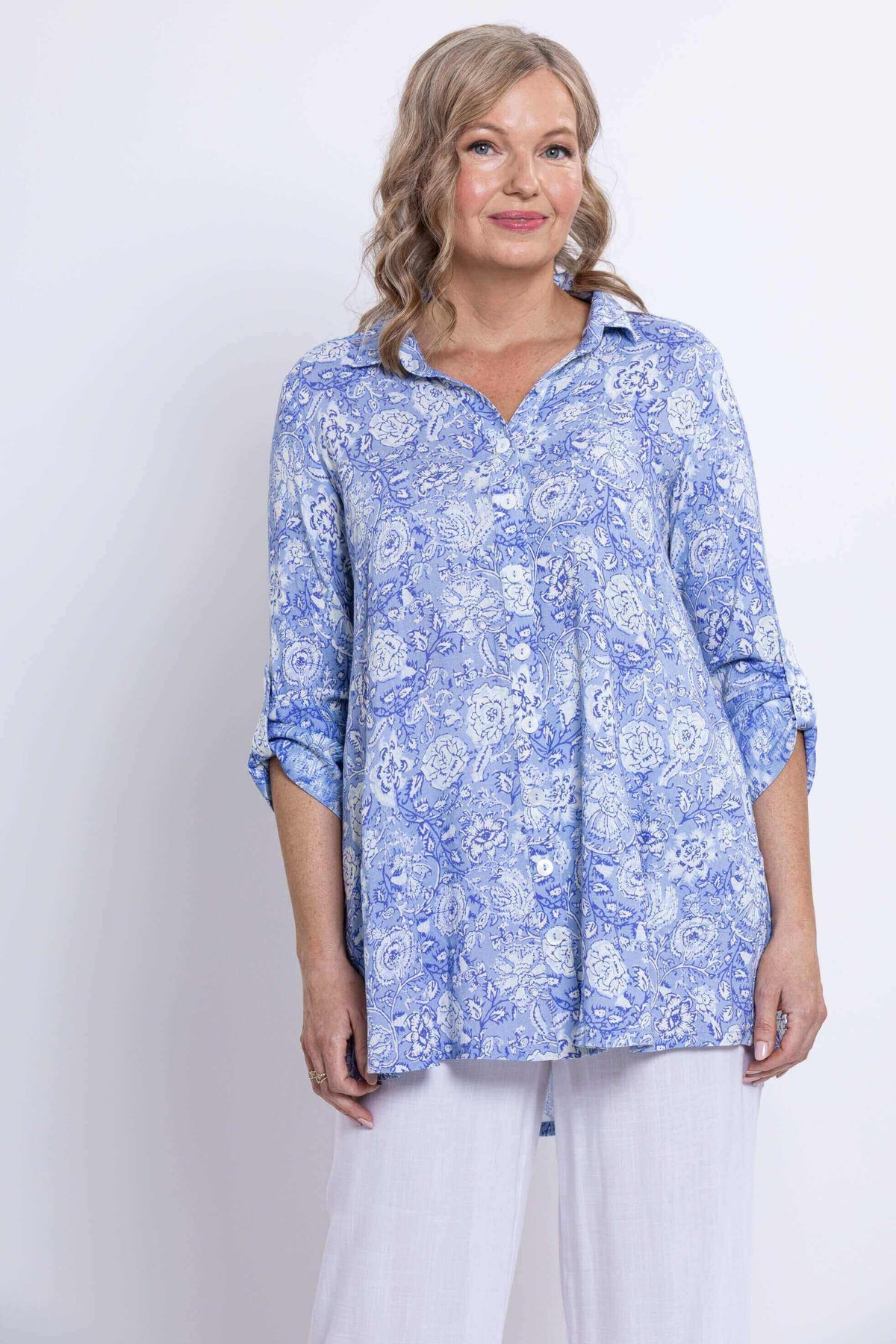 Medium shot of woman in blue paisley tunic with button-up front and white pants
