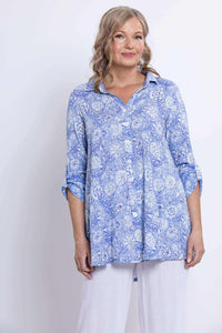 Medium shot of woman in blue paisley tunic with button-up front and white pants
