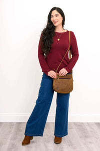 Woman styled in merlot boat neck top, jeans, brown crossbody bag, and boots