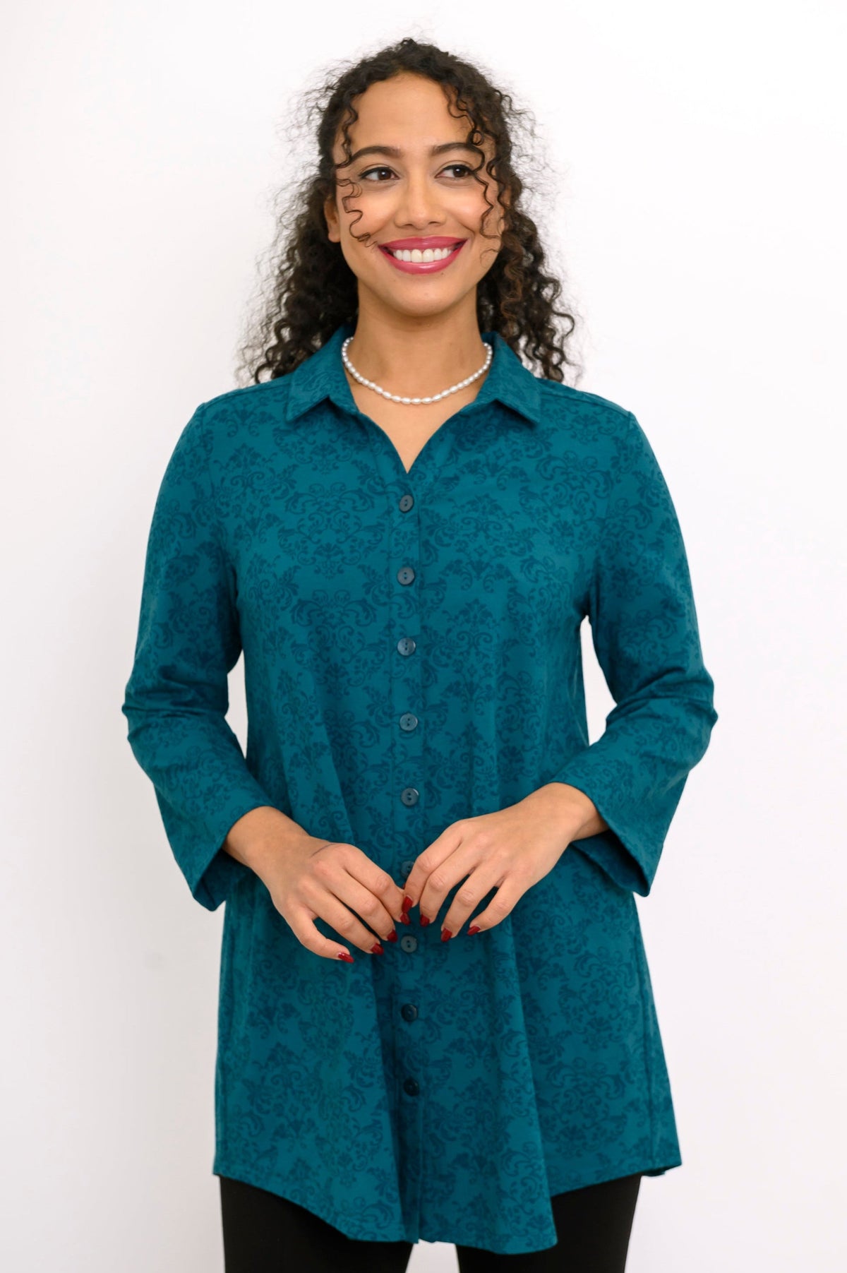 Teal patterned long-sleeve knit shirt buttoned up and accessorized with a pearl necklace, shown in a front view.