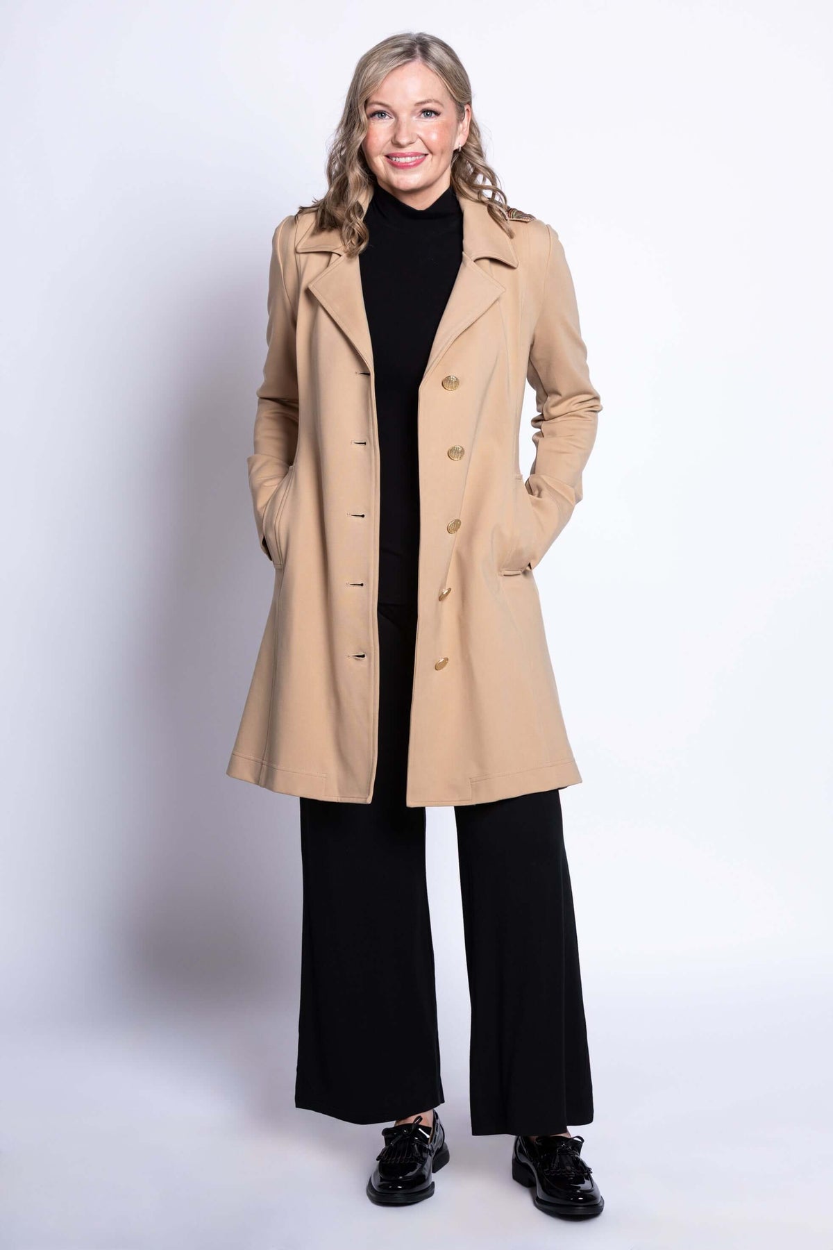 Smiling woman in tan modal trench jacket with hands in pockets