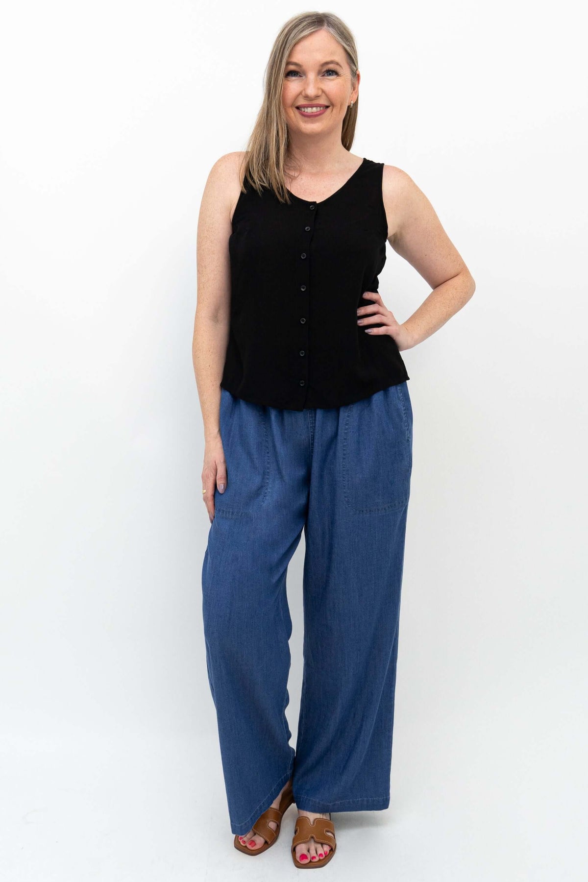 Smiling woman modeling wide-leg blue Tencel denim pants and black sleeveless shirt