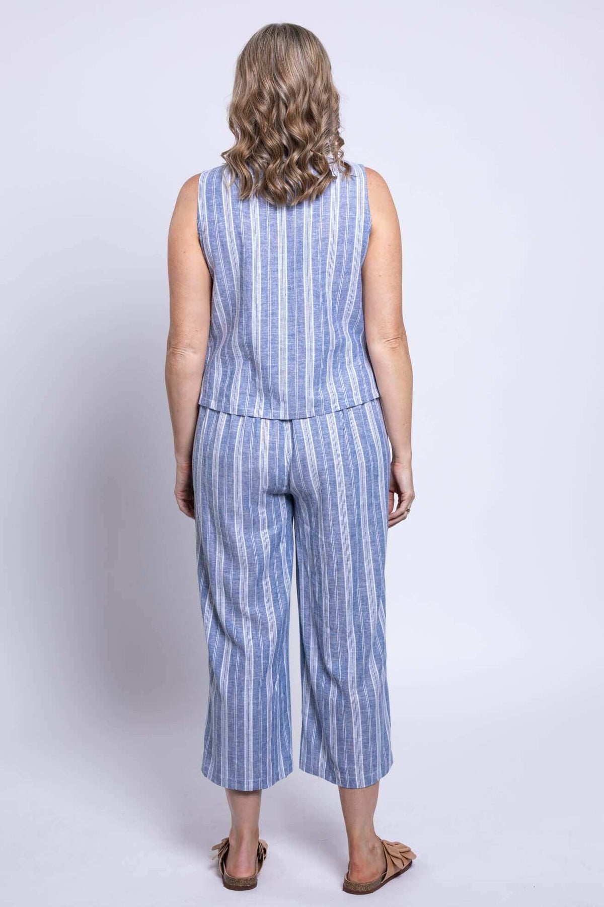Full body back view of woman modelling matching tank top and pants with blue and white stripes