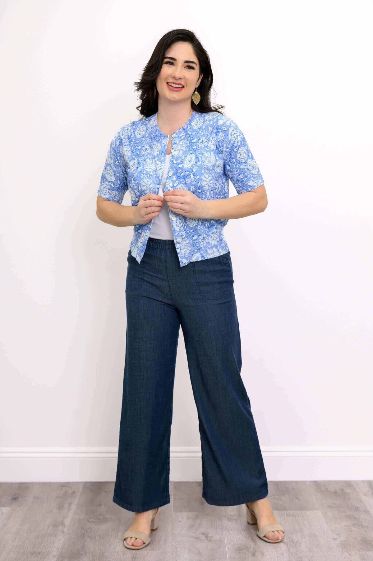 Model buttoning up Shen short-sleeve blue floral cardigan, smiling