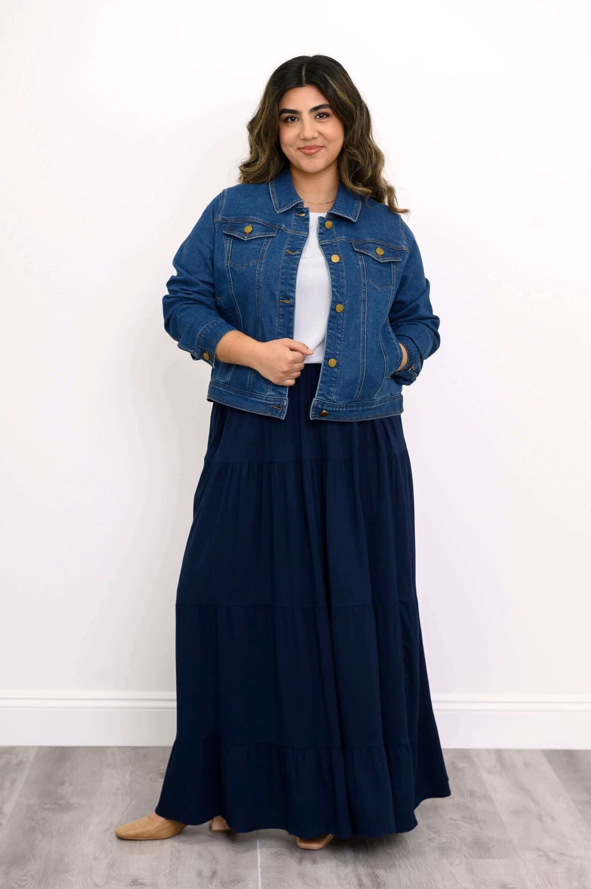 Model confidently posing in denim jacket with gold buttons and a long navy blue skirt