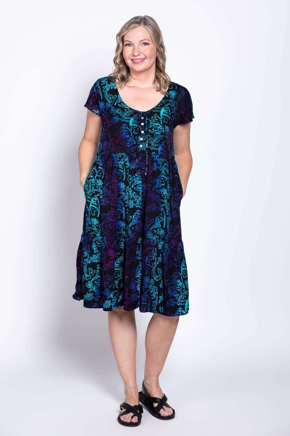 Model showing dress pockets in a black, teal, and purple tiered dress with flutter sleeves