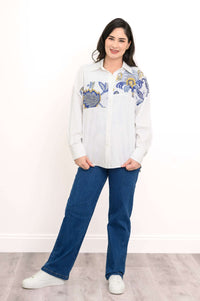 Model facing forward in white blouse with blue floral print and jeans