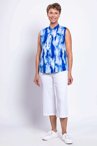 Woman facing forward wearing a blue tie-dye sleeveless blouse and white cropped pants
