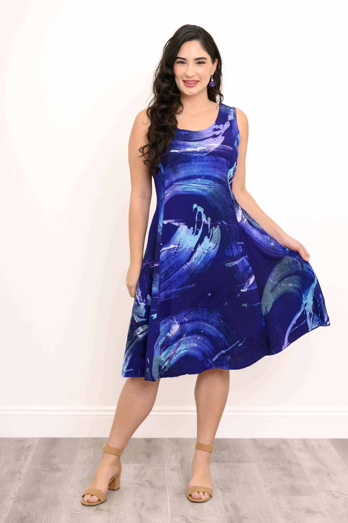 Model holding hem of vibrant blue sleeveless dress with artistic print