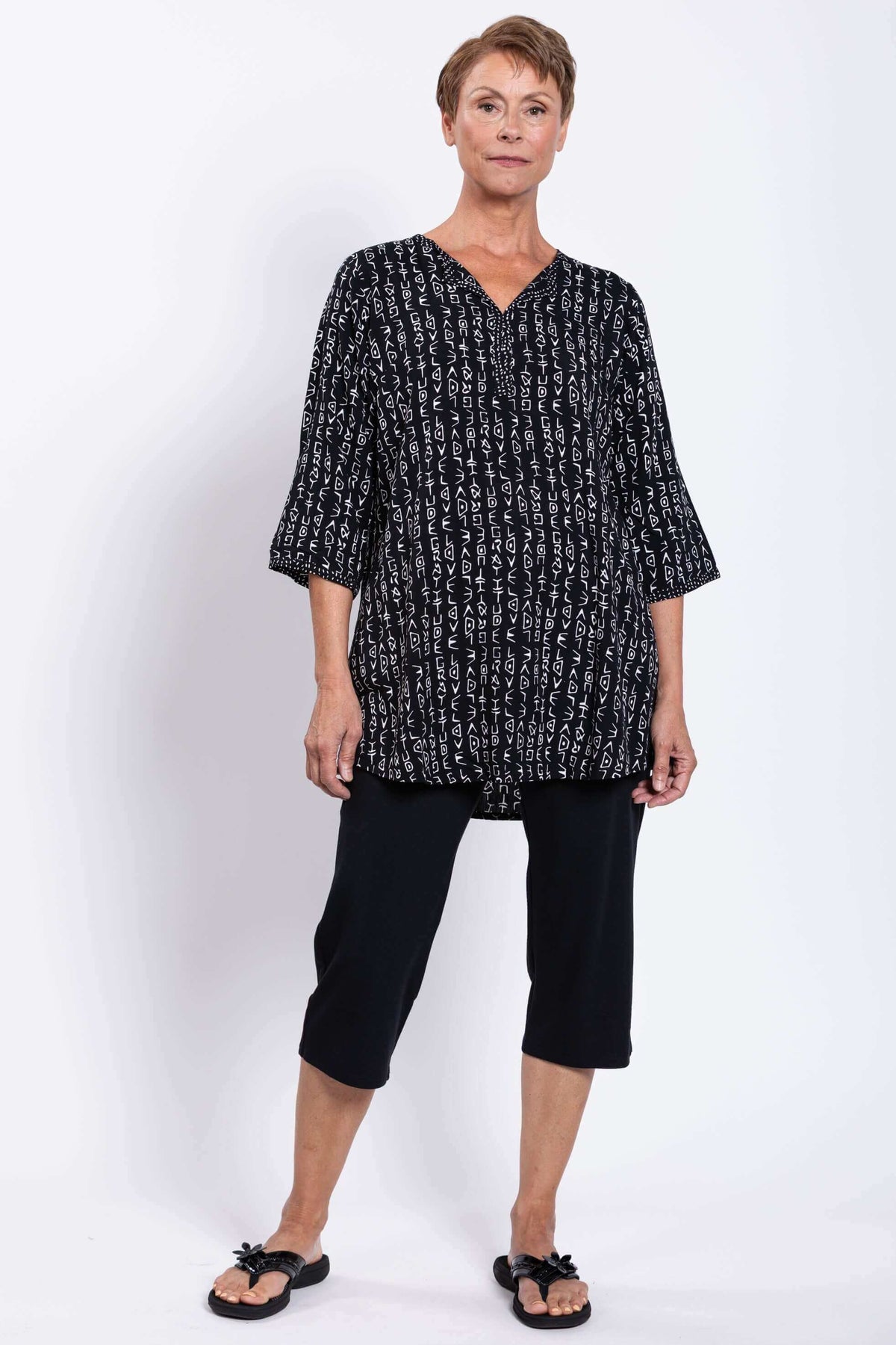 Woman modeling black tunic with white print and cropped black pants