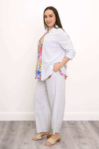 Full body side view of woman wearing white button up shirt over a floral top and barrel leg trousers