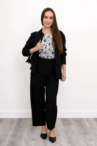 Full body view of woman wearing a black purse, black pants, and black button-up shirt on a floral print top