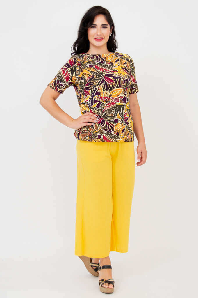 Second model in botanical boatneck tee and yellow pants, standing and smiling