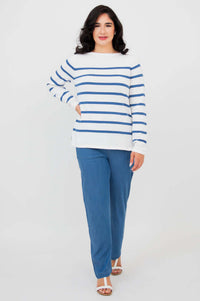 A woman standing with hand on hip in a striped white and blue sweater and blue pants