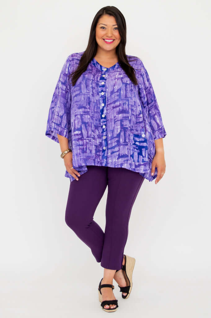 Model in purple patterned tunic with playful stance and purple pants