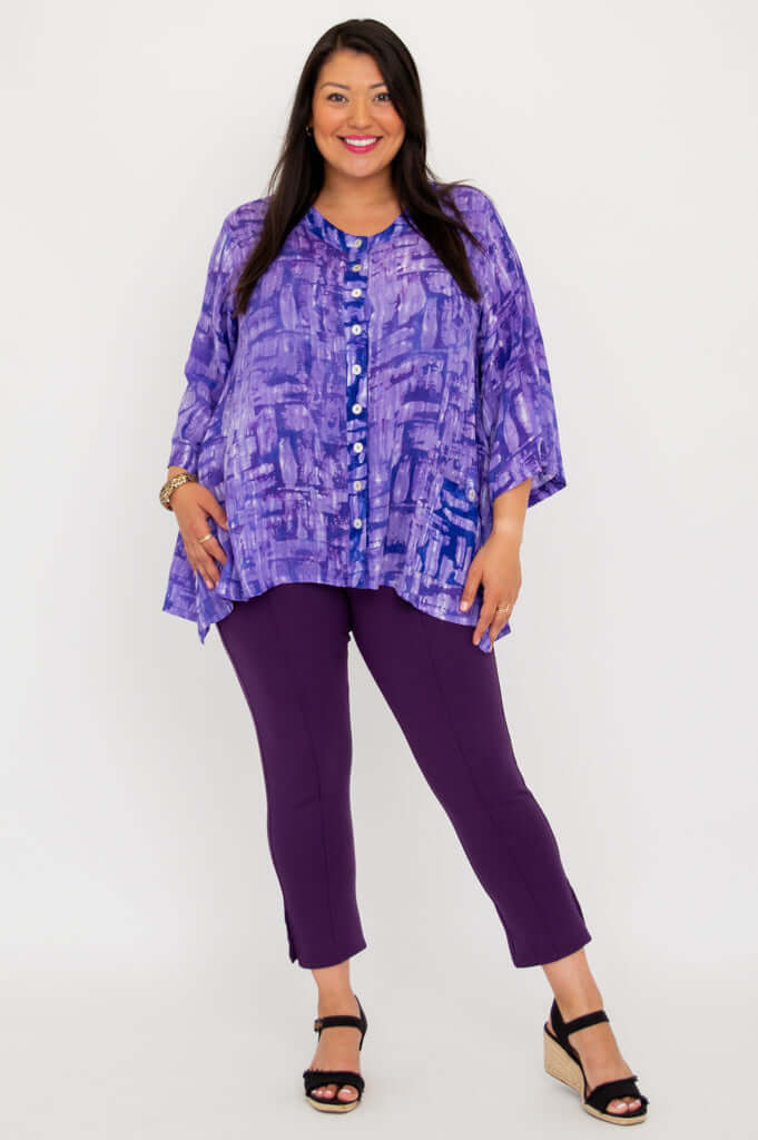 Model posing in purple V-neck tunic and purple pants, angled stance