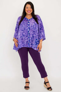 Model posing in purple V-neck tunic and purple pants, angled stance