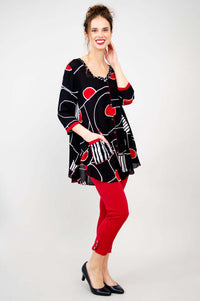 Model in batik art top with left hand in striped pocket, red pants, and black heels