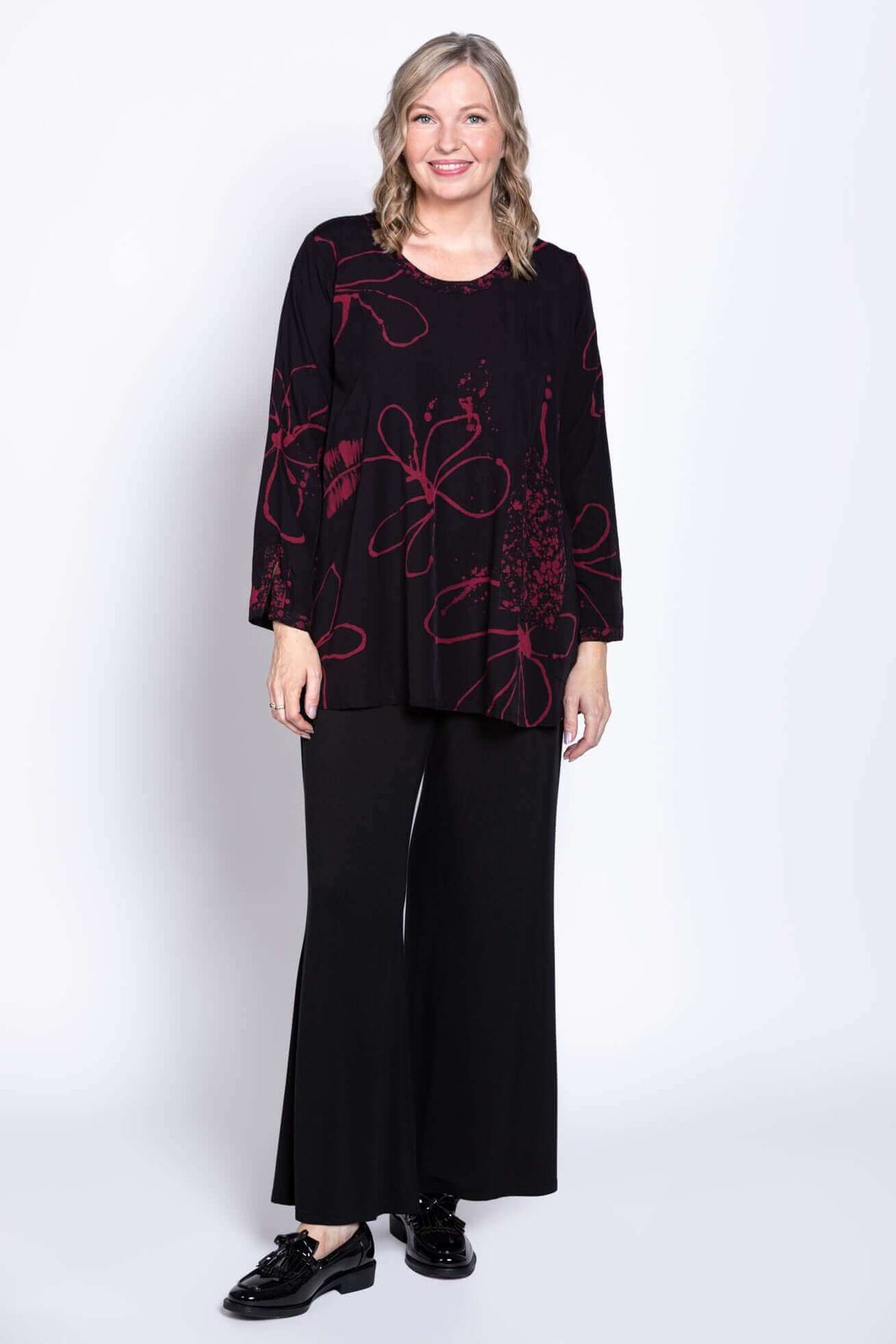 Model in black blouse with berry pattern, facing forward, wide-leg pants visible
