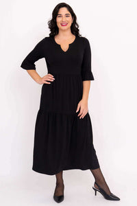 Model in black midi dress with ruffle sleeves and hand on hip, showing front detail