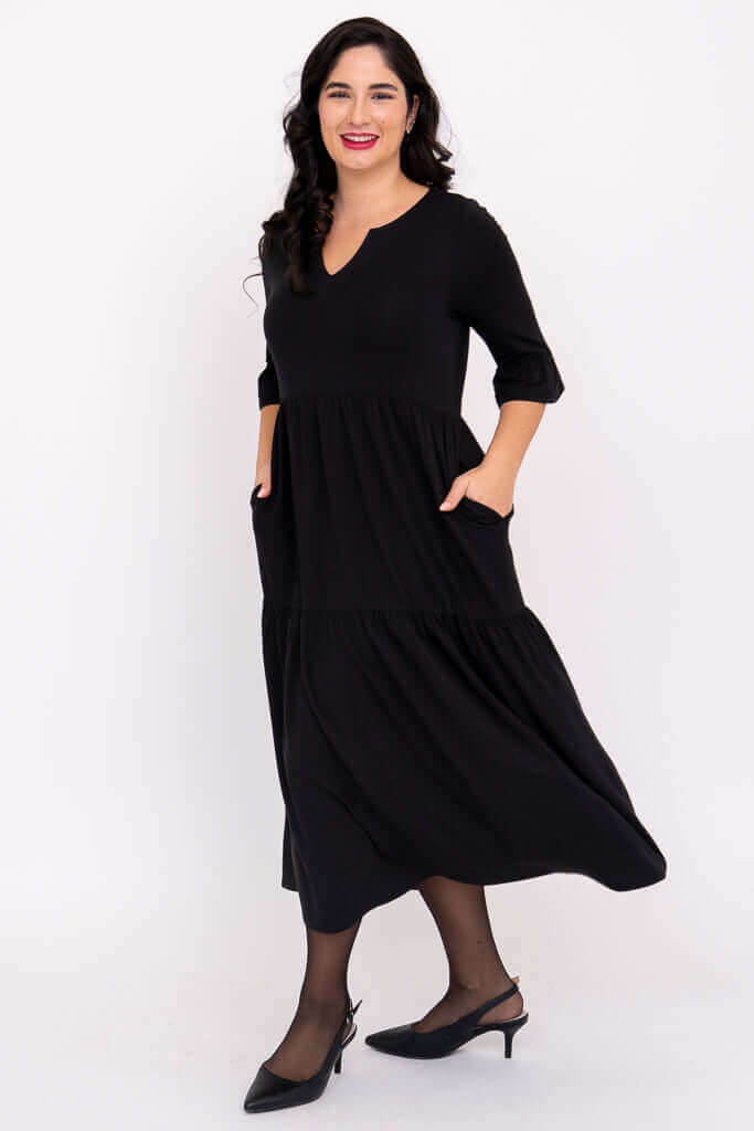 Model in motion wearing black tiered midi dress with hands in pockets and ruffle sleeves