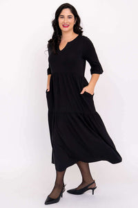 Model in motion wearing black tiered midi dress with hands in pockets and ruffle sleeves