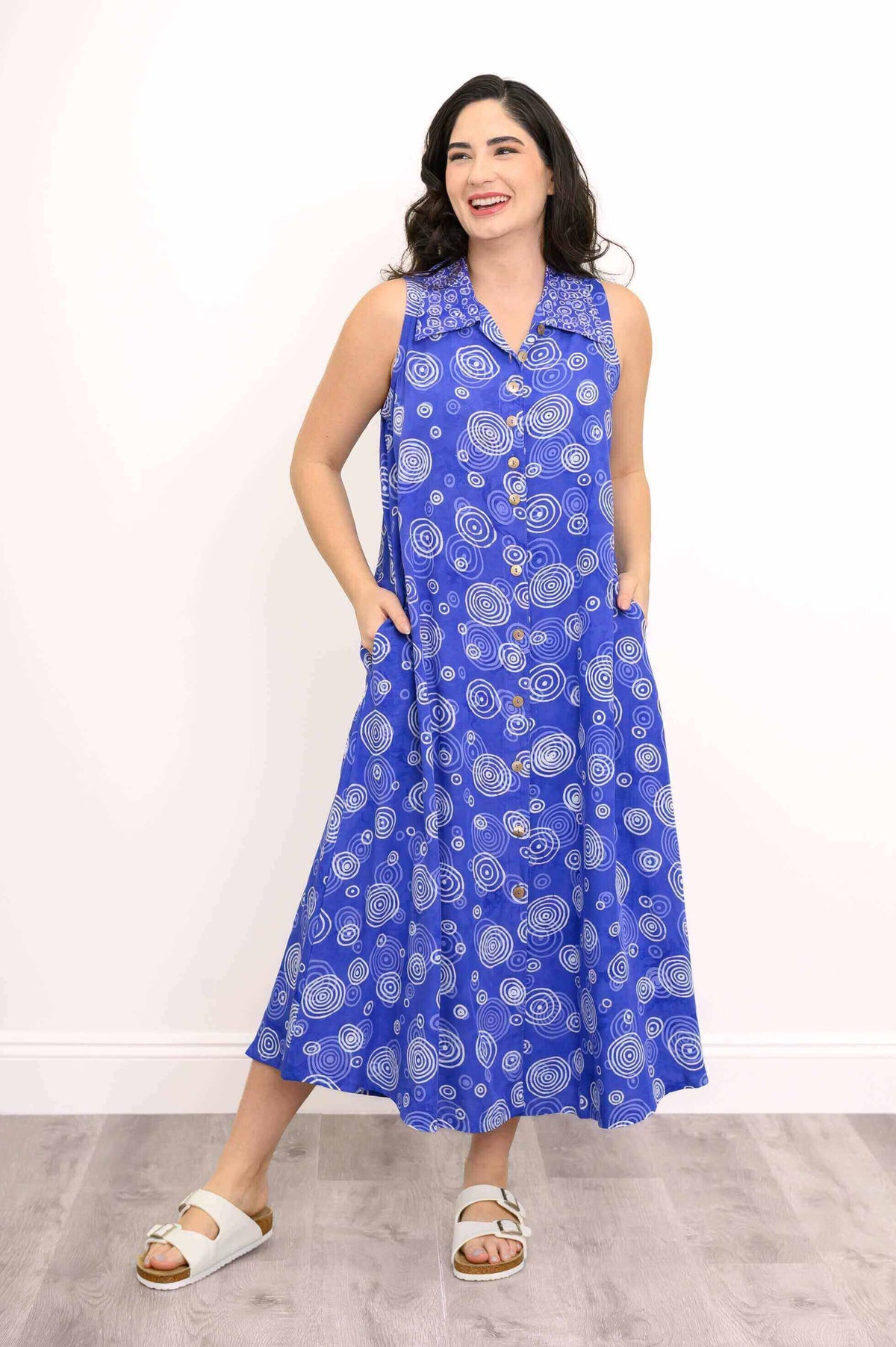 Model hands in pockets wearing a blue A-line sleeveless dress with white circular swirl designs