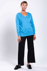 Woman modeling a blue V-neck sweater and black pants, standing with a relaxed pose